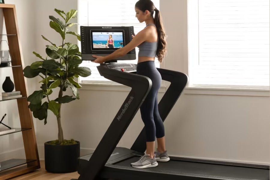 Woman in gray sports bra and black leggings using NordicTrack treadmill with interactive screen display in home setting