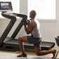 Man performing lunge exercise on black NordicTrack treadmill with touchscreen display in bright home gym