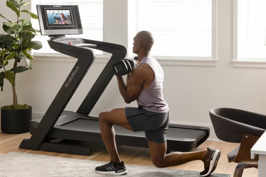 Man performing lunge exercise on black NordicTrack treadmill with touchscreen display in bright home gym