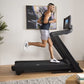 Man running on black NordicTrack treadmill with digital display in home gym setting, wearing white sneakers and gray shorts