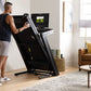 Man in black sleeveless shirt and shorts using NordicTrack 1250 treadmill with touchscreen display in modern living room sett