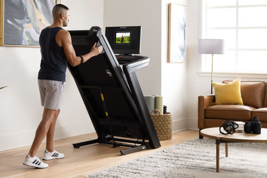 Man in black sleeveless shirt and shorts using NordicTrack 1250 treadmill with touchscreen display in modern living room sett
