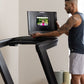 Man wearing navy tank top using black NordicTrack treadmill with display screen showing workout video