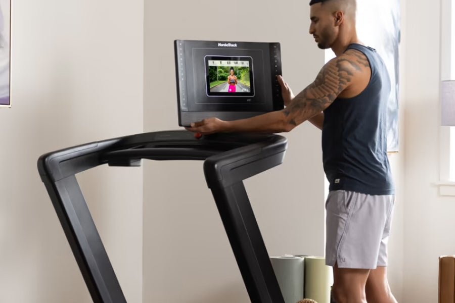 Man wearing navy tank top using black NordicTrack treadmill with display screen showing workout video