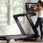 Woman in white tank top and black leggings running on black NordicTrack treadmill with blue accents in bright home gym