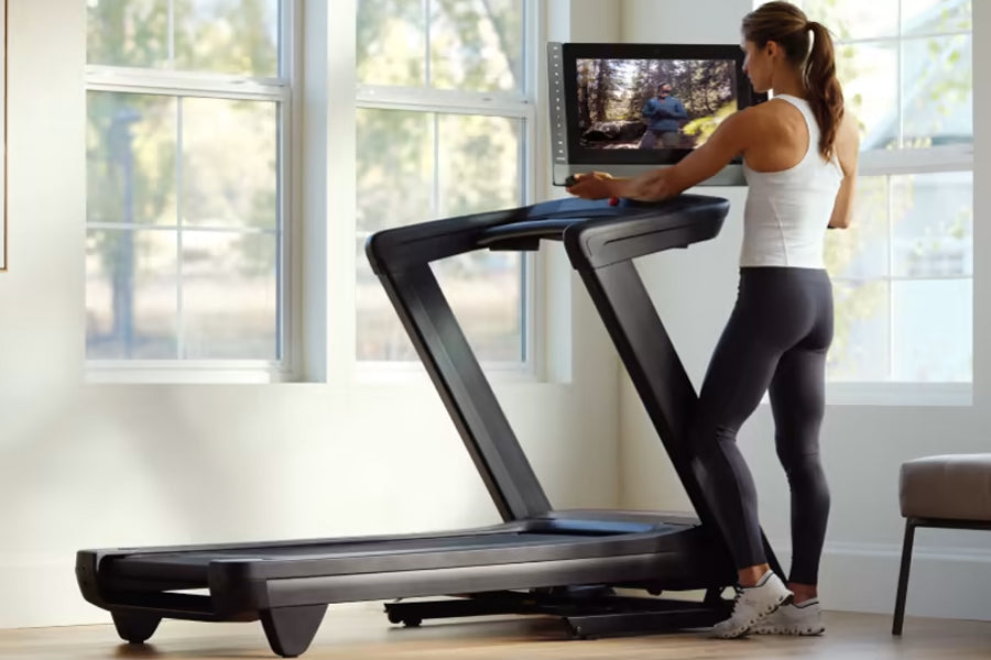Woman in white tank top and black leggings running on black NordicTrack treadmill with blue accents in bright home gym