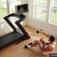 Black NordicTrack treadmill with curved running surface and touchscreen display, shown in home gym setting with person doing 