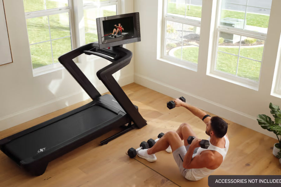 Black NordicTrack treadmill with curved running surface and touchscreen display, shown in home gym setting with person doing 
