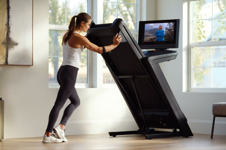 Woman using black NordicTrack treadmill with touchscreen display in bright home gym with large windows