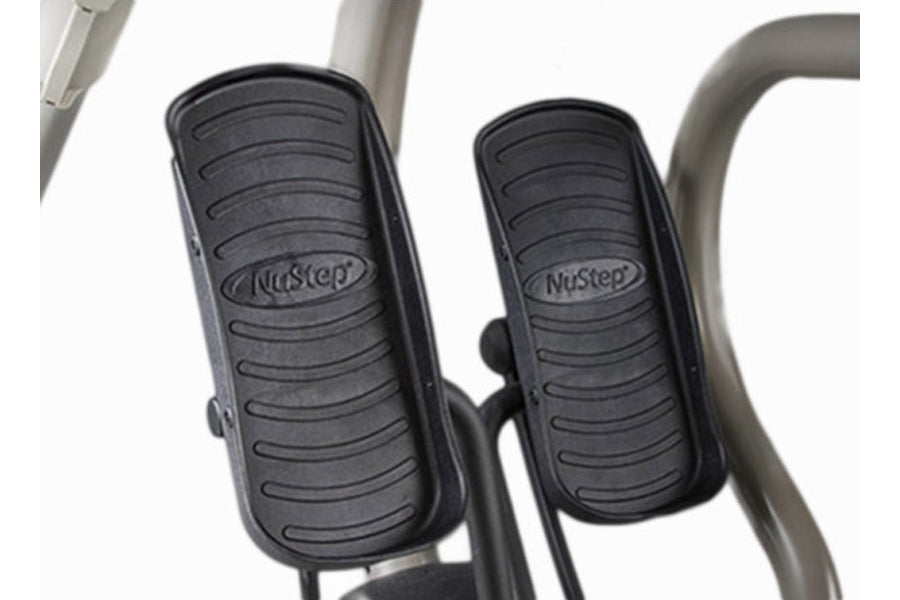Black rubber pedals with NuStep branding on recumbent elliptical stepper, white background