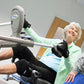Senior woman using NuStep T5XR recumbent elliptical stepper with green handles and black foot pedals, assisted by trainer in 