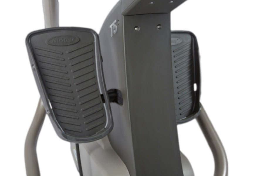 NuStep T5 recumbent elliptical stepper with gray frame, black foot pedals with ribbed texture, and beige handles on white bac