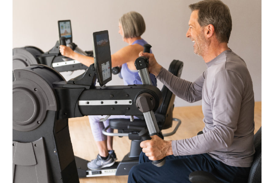 Man and woman using black NuStep UE8MAX upper body ergometer with tablet display and resistance handles in home gym setting