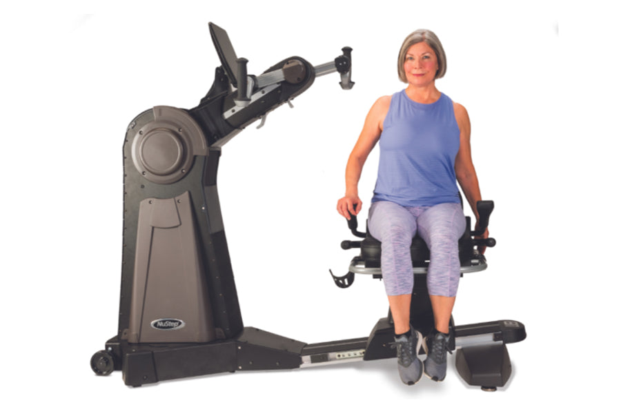 Woman using NuStep UE8PRO upper body ergometer with gray and black frame, demonstrating seated exercise motion on white backg