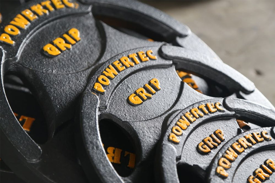 Powertec Olympic weight plates in gray with yellow text and grip handles, stacked in flat lay view