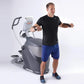 Man wearing black t-shirt and blue shorts exercising on Octane Q47x gray and white elliptical machine against white backgroun