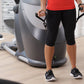 Person wearing red tank top and black capri leggings using gray and white elliptical machine in home gym setting