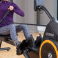 Woman in purple jacket and gray leggings using black and orange Octane RO rowing machine indoors
