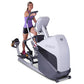 Woman wearing purple sports tank top and black shorts using white and gray elliptical trainer machine on white background
