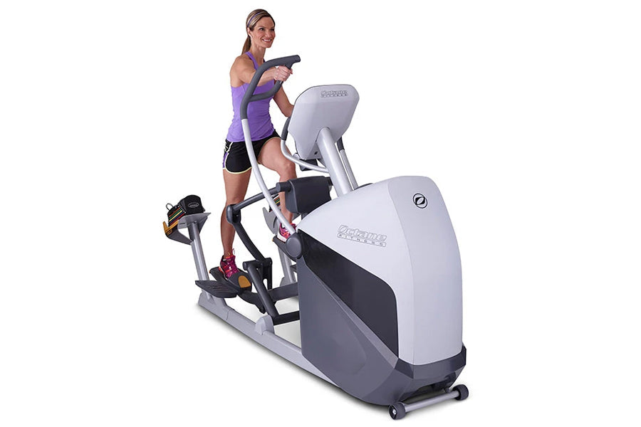 Woman wearing purple sports tank top and black shorts using white and gray elliptical trainer machine on white background