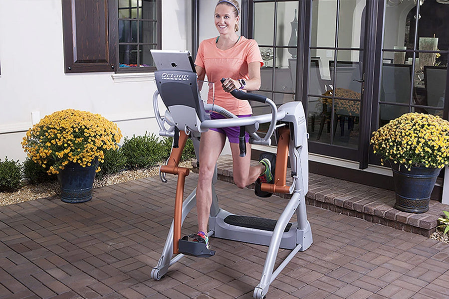 Woman in coral t-shirt and purple shorts using white and gray Octane Fitness ZR7 Zero Runner exercise machine on patio with y