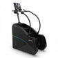 Black commercial stair climbing machine with blue accent stripe, digital display console, and dual handrails, on white backgr