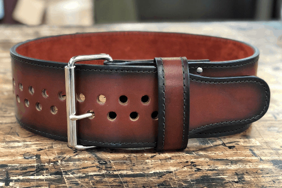 Brown leather power belt with metal stud details and silver buckle, flat lay on wood surface