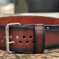 Brown leather belt with black edges and silver buckle, featuring double row of brass grommets, displayed on wooden surface