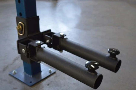 Warrior Power Rack Double Landmine Attachment with two black cylindrical tubes, gold accents, and blue vertical post on concr
