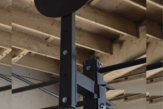 Black metal wall ball target attachment mounted on power rack post with bolted bracket connection, showing exposed wood beam 