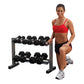Woman in red sports bra and black shorts posing next to two-tier dumbbell rack with black hex dumbbells on white background