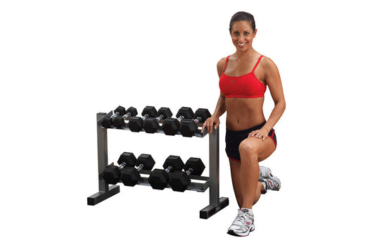 Woman in red sports bra and black shorts posing next to two-tier dumbbell rack with black hex dumbbells on white background