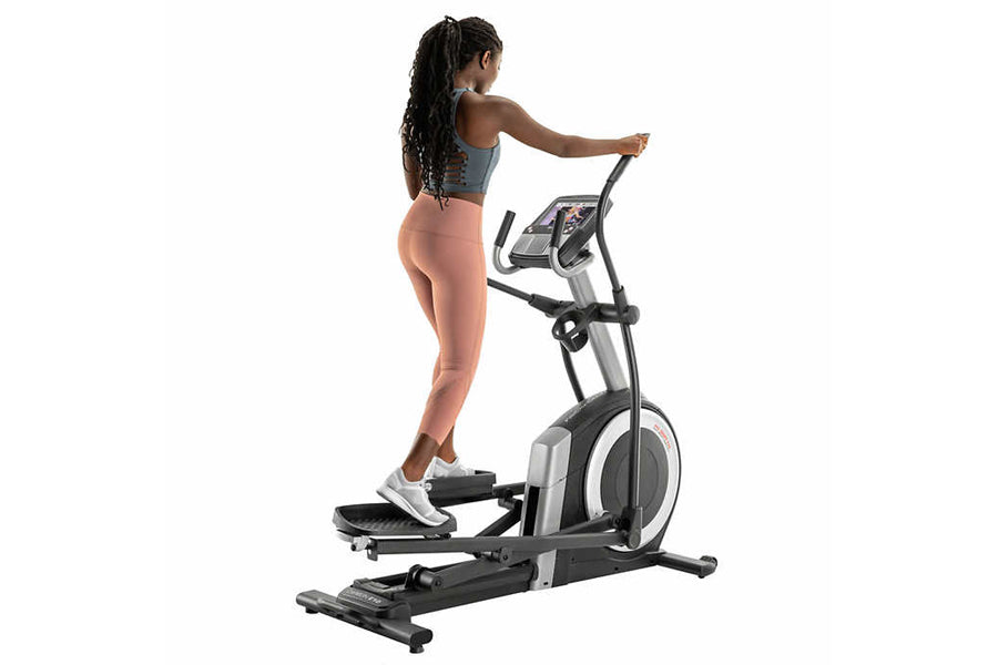 Woman exercising on ProForm Carbon E10 elliptical machine with gray and black frame, worn against white background