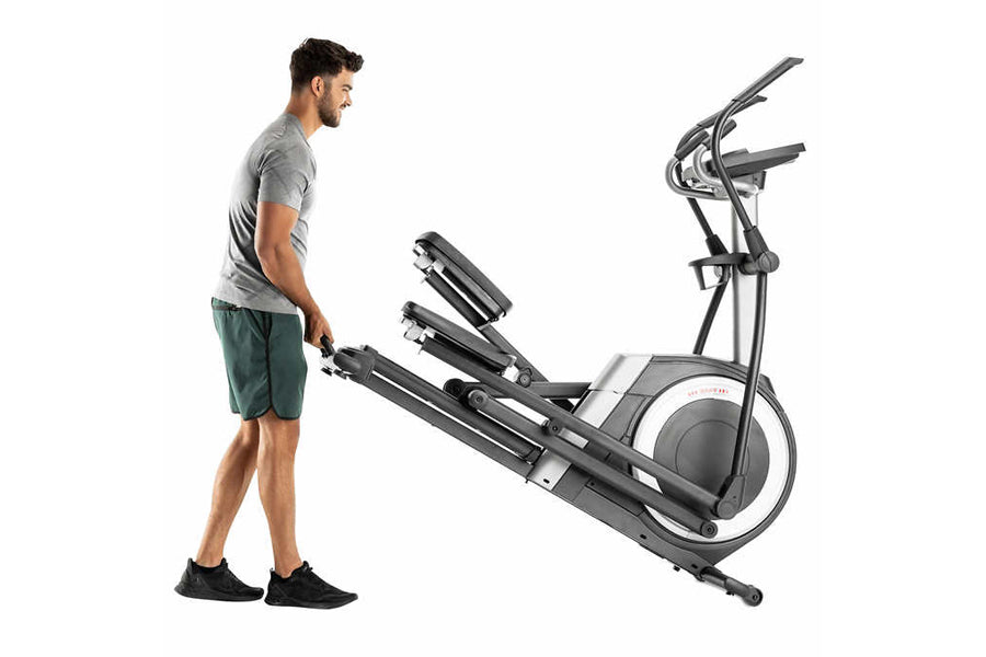 Man in gray shirt standing next to black and silver elliptical machine with digital display on white background