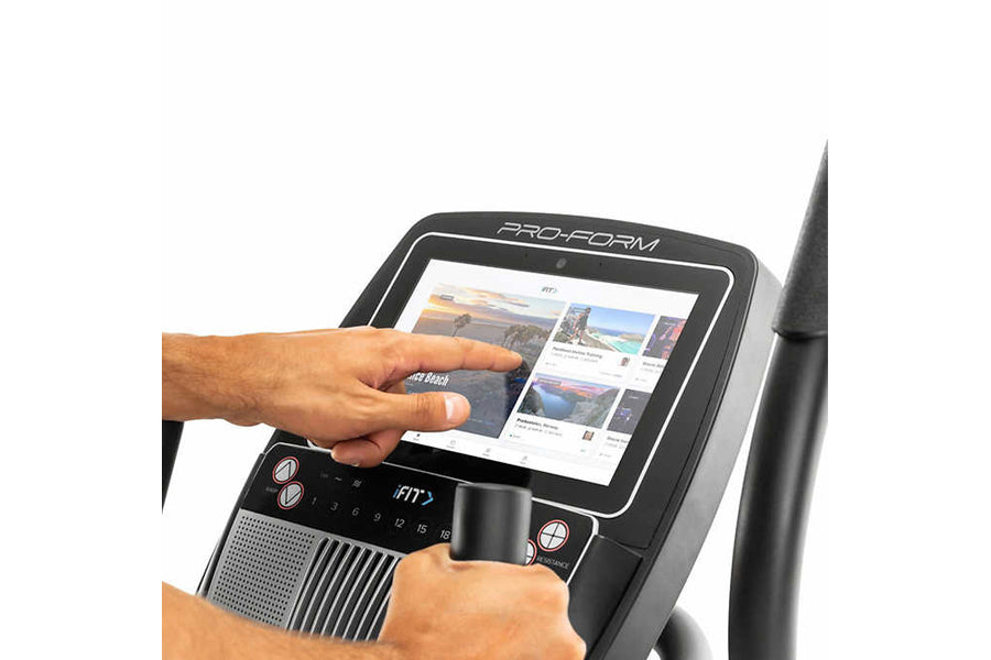 User's hands operating ProForm Carbon E10 elliptical console with touchscreen display showing workout content