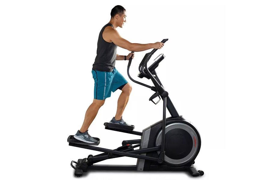 Man using black and gray ProForm Carbon EL elliptical machine, wearing teal shorts and black tank top on white background
