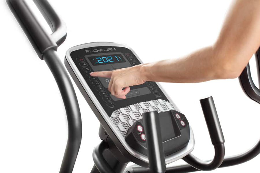 Hand operating digital console on ProForm Carbon EL elliptical with blue display and black controls, worn by user on white ba