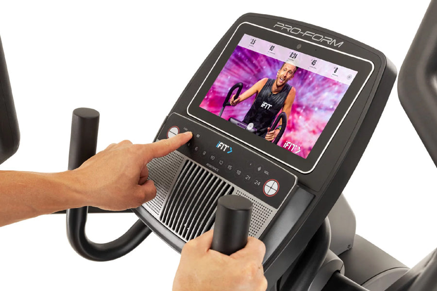 ProForm Carbon HIIT H10 elliptical with touchscreen display showing workout video, black frame with handlebars, user's hands 