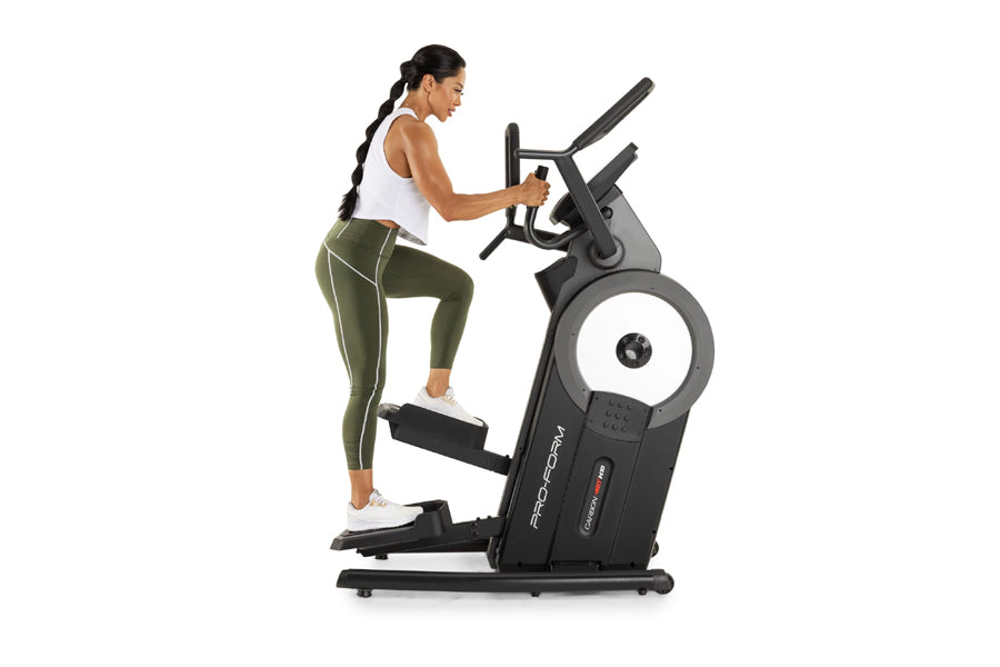 Woman in white tank top and olive green leggings using black ProForm elliptical machine on white background