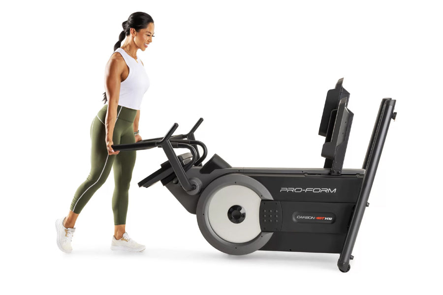 Woman in white tank top and olive leggings using black ProForm Carbon HIIT H10 elliptical machine on white background