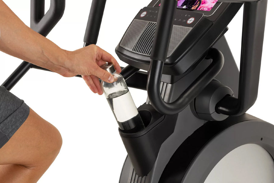 Person holding water bottle on black and gray ProForm elliptical machine with digital display