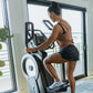 Woman wearing tan tank top and black shorts using white and black elliptical machine indoors