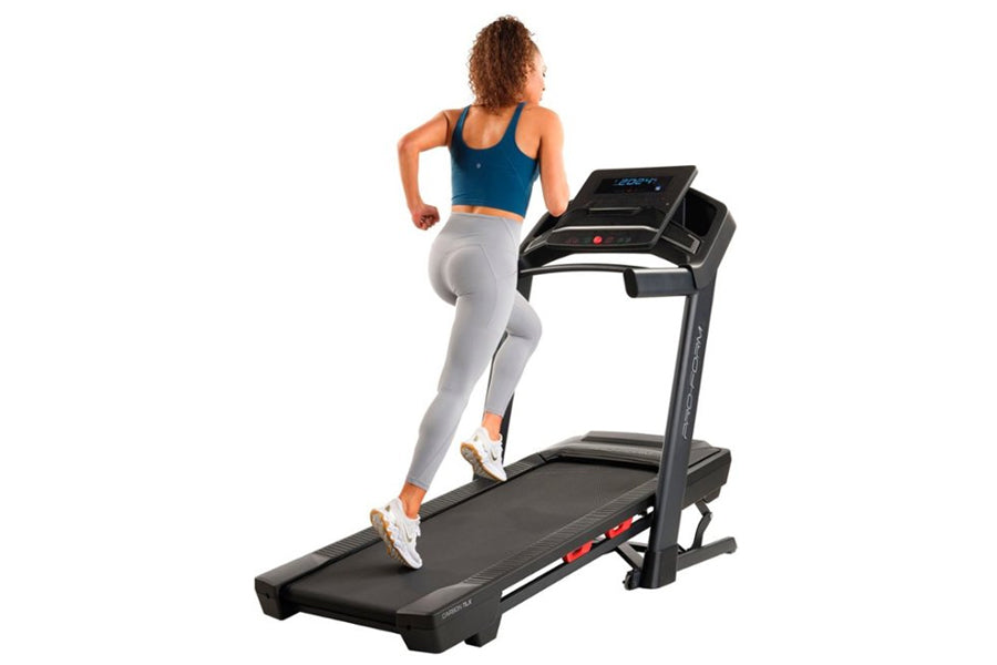 Woman running on ProForm Carbon TLX black treadmill with digital display, wearing blue sports bra and gray leggings