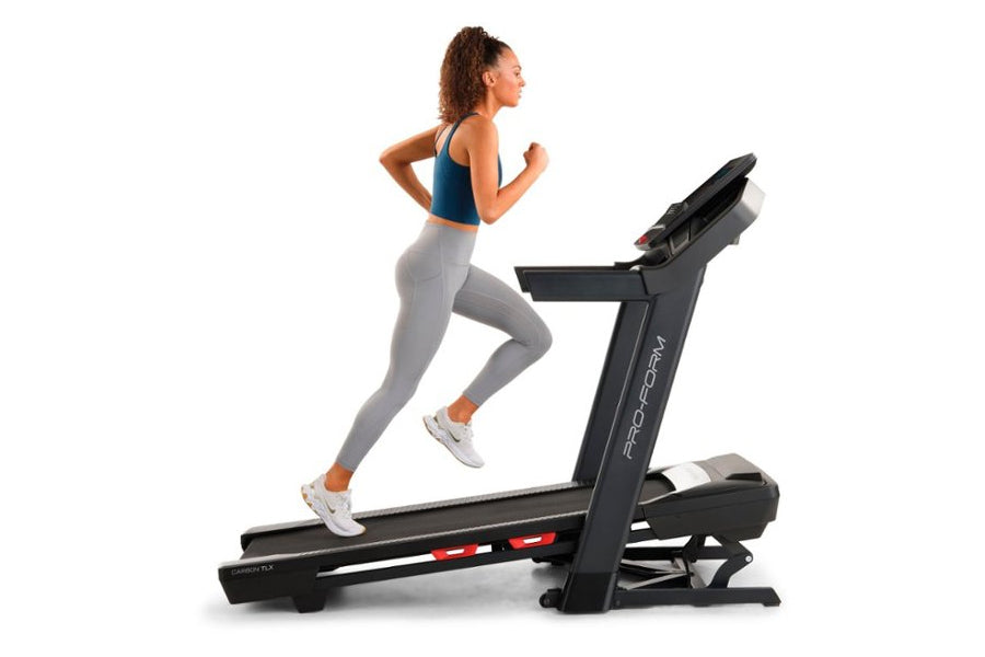 Woman running on black ProForm Carbon TLX treadmill, wearing blue sports bra and gray leggings, on white background
