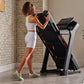 Woman in white crop top and shorts using black and silver ProForm treadmill in home gym with brick wall