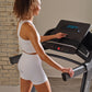 Woman in white sports bra and shorts using black and silver ProForm treadmill with digital display in home gym setting