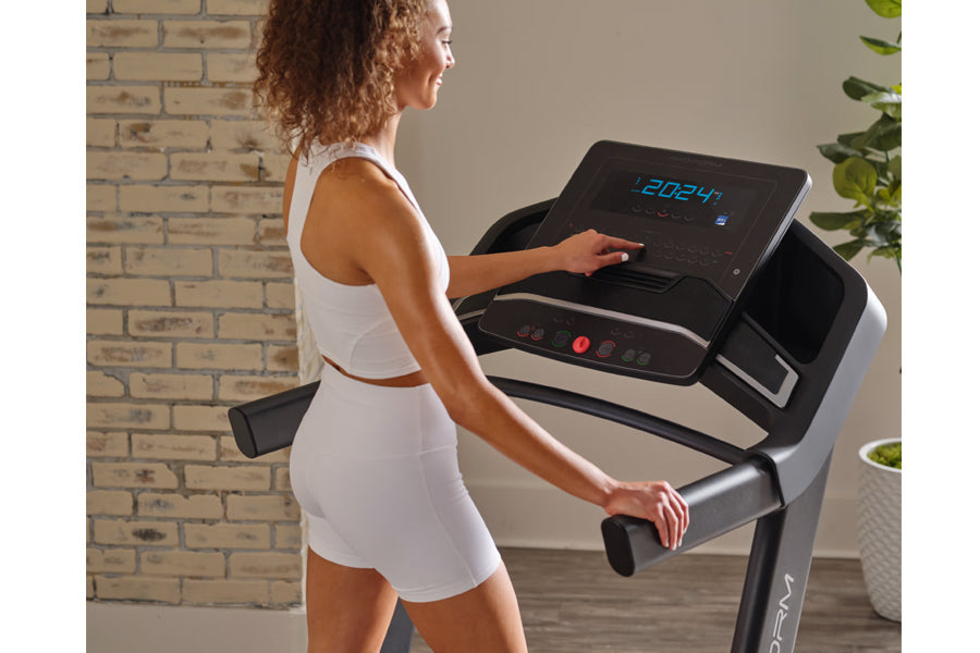 Woman in white sports bra and shorts using black and silver ProForm treadmill with digital display in home gym setting