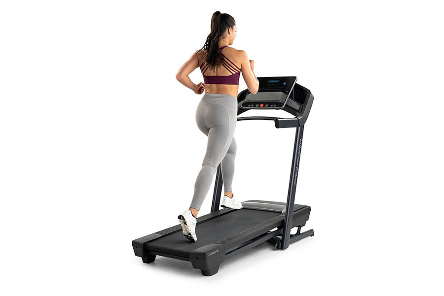 Woman in burgundy sports bra and gray leggings running on black ProForm treadmill with digital console, white background