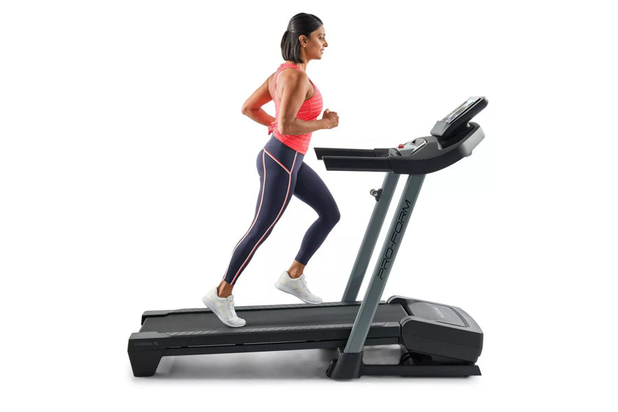 Woman running on black ProForm treadmill wearing coral sports bra and navy leggings with white sneakers