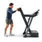 Man in navy shirt and gray shorts using black ProForm treadmill with digital display on white background